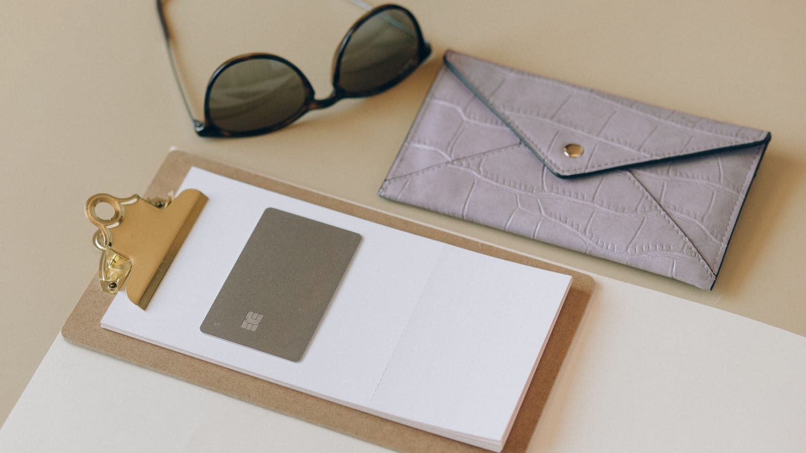A leather wallet and sunglasses laid out on a desk
